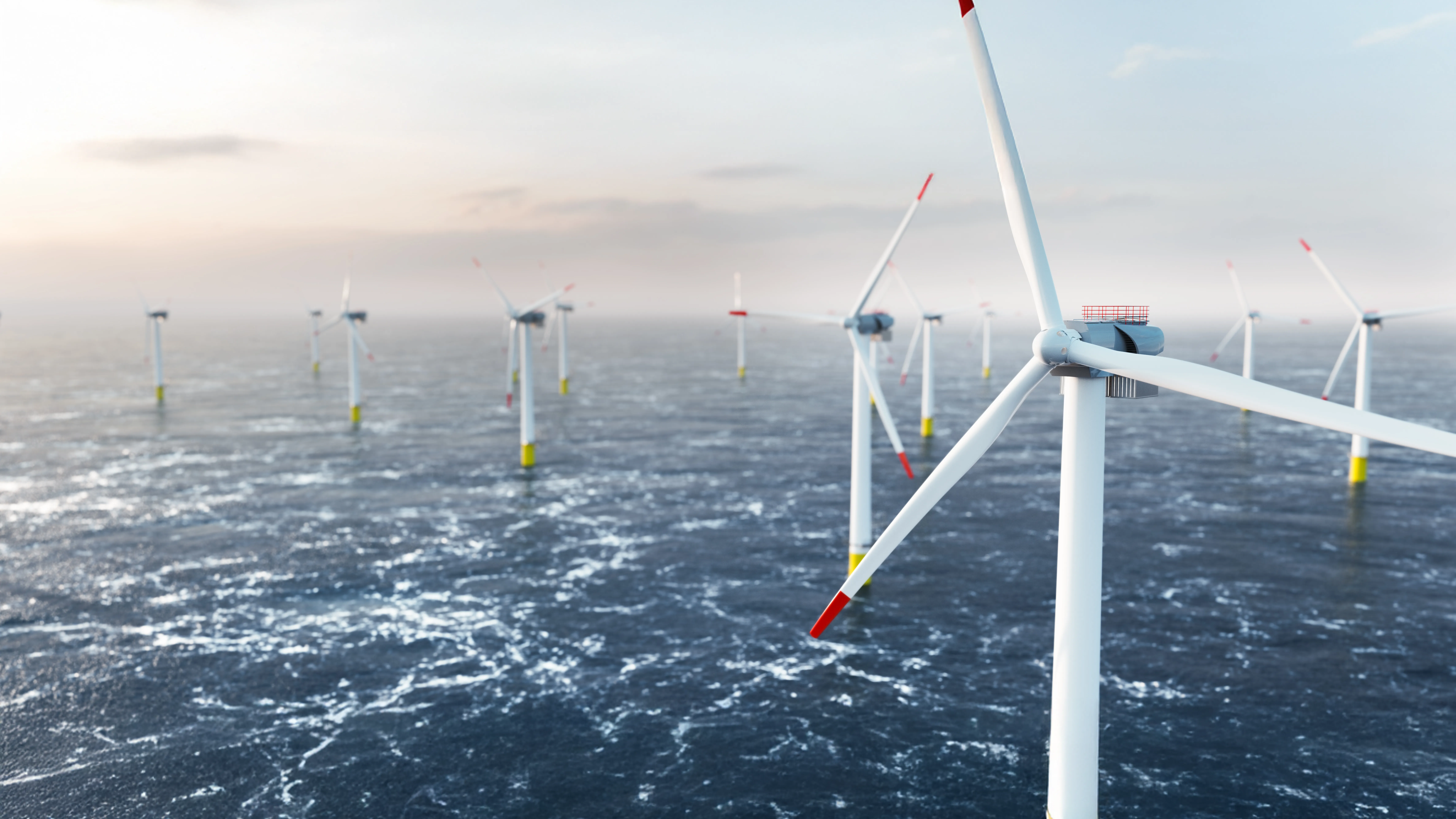 Offshore wind farm with multiple large wind turbines in the ocean under a cloudy sky at sunset.